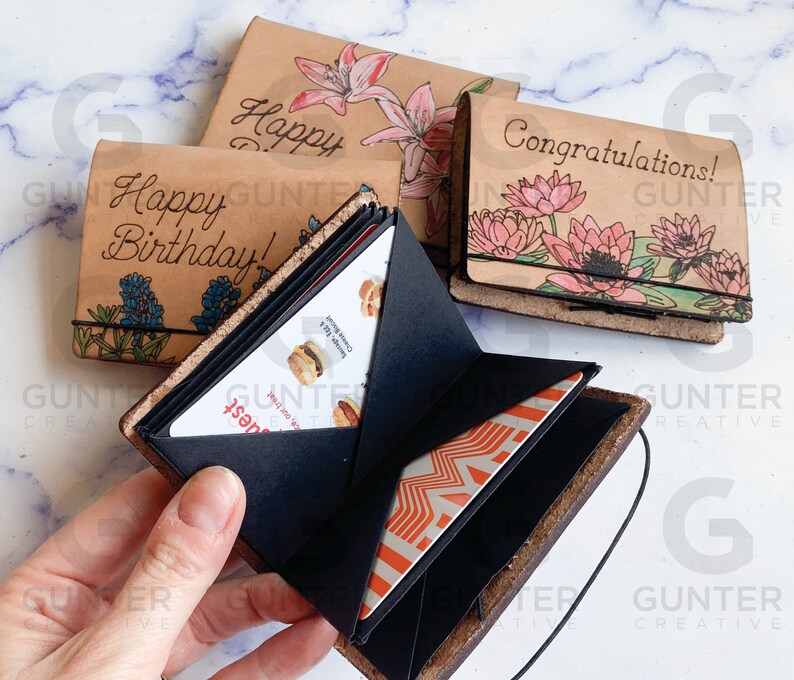 May include: A set of three leather-bound journals with floral designs and personalized messages. The journals are open to reveal a black gift card holder with a gift card inside.