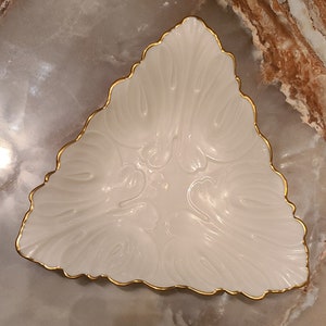 May include: A white porcelain triangular dish with a gold rim and a floral design.