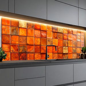 May include: A kitchen backsplash with a mosaic of orange, brown, and gold square tiles. The tiles have a textured, cracked appearance. A black tap and dark grey cabinets are visible.