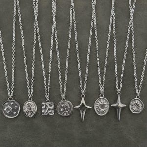 以下が含まれることがあります： 太陽、星、コインのような形など、さまざまなペンダントデザインのシルバーカラーのネックレスのコレクション。ペンダントは繊細なチェーンから吊り下げられており、ミニマリストで天体的な美しさを生み出しています。