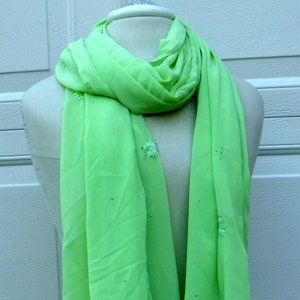May include: A lime green sheer scarf with white embroidered flowers. The scarf is draped over a white mannequin.