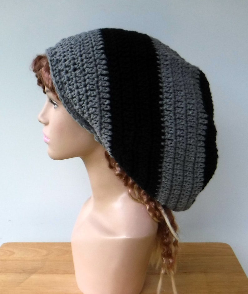 May include: A handmade crochet beanie in a striped pattern of black and gray. The hat is shown on a mannequin head, showcasing the texture and design of the knitted fabric. The beanie is a stylish accessory.