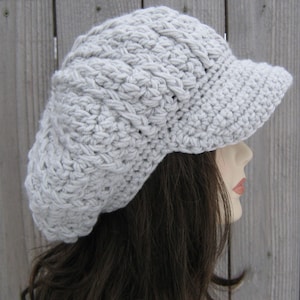May include: A gray crocheted beanie with a brim. The beanie has a textured, cable knit design.