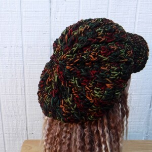 May include: A crocheted beanie in a multi-colored pattern of brown, green, and orange. The beanie has a slightly curved brim.