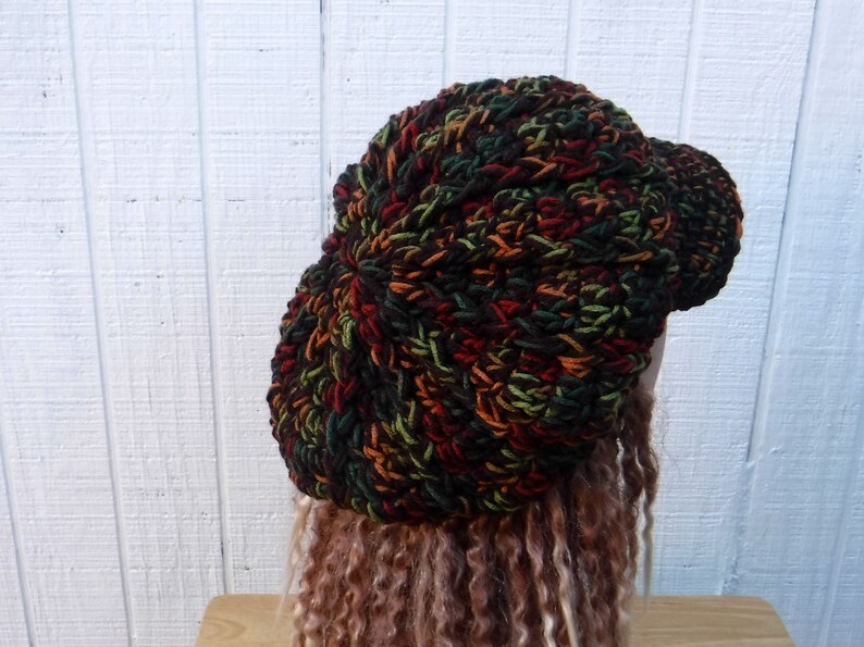 May include: A crocheted beanie in a multi-colored pattern of brown, green, and orange. The beanie has a slightly curved brim.