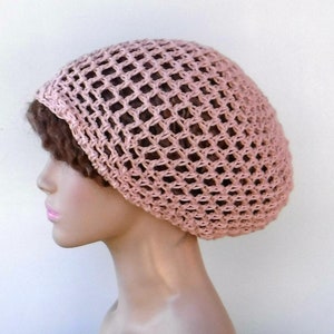 May include: A light pink crocheted hat with a net-like design. The hat is worn on a mannequin head, showcasing its shape and texture. The open weave allows a glimpse of the hair beneath, creating a delicate and airy appearance.