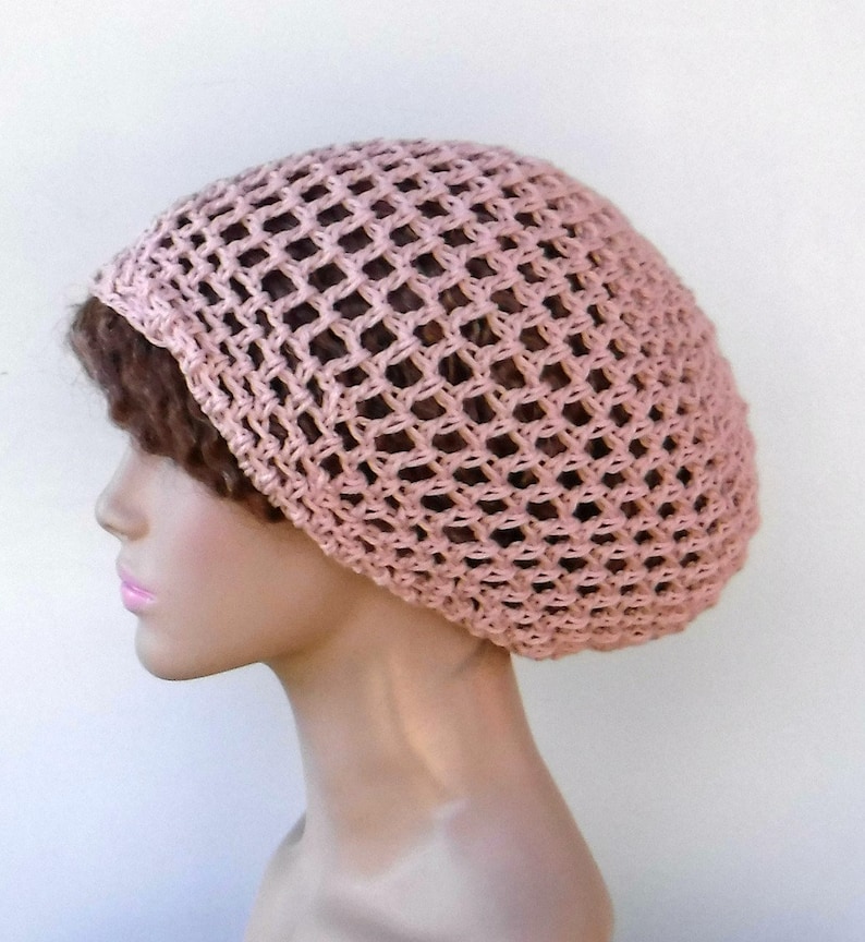 May include: A light pink crocheted hat with a net-like design. The hat is worn on a mannequin head, showcasing its shape and texture. The open weave allows a glimpse of the hair beneath, creating a delicate and airy appearance.