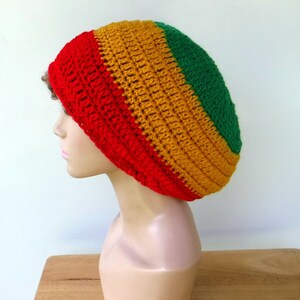 May include: A red, gold, and green crocheted beanie hat. The hat is made with a thick yarn and has a slouchy fit.