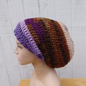 May include: A slouchy crochet beanie featuring a gradient of colors starting with light purple at the brim, transitioning into deep violet, dark brown, and copper, and ending with a light beige tone at the crown, crafted with a textured stitch pattern.