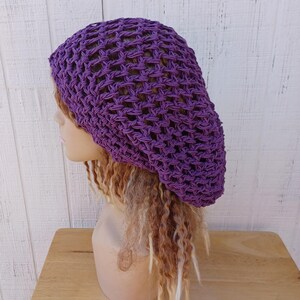 May include: Purple crochet beanie hat with a loose, open weave. The hat is shown on a mannequin with long, blonde dreadlocks.