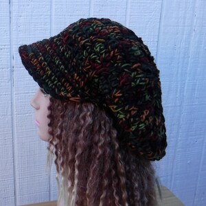 May include: A black, green, and orange crocheted beanie with a wide brim. The beanie is slouchy and has a casual, relaxed style.