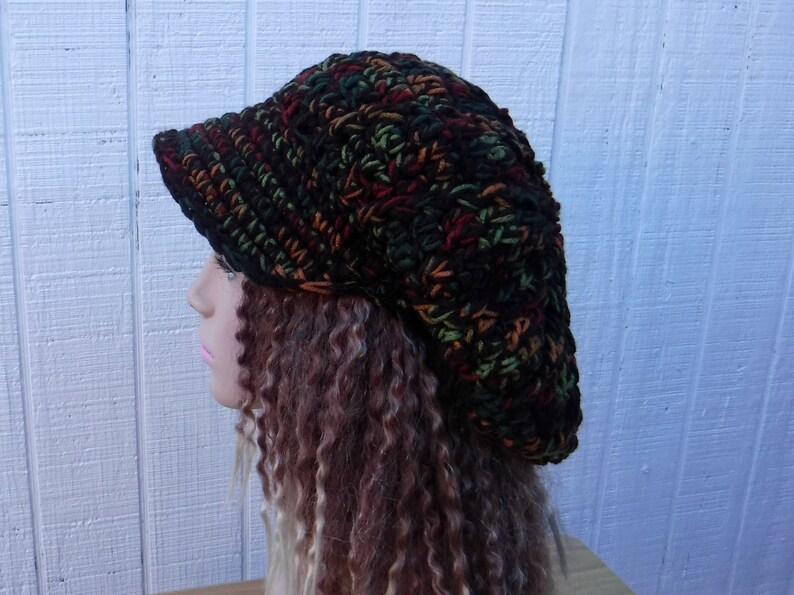 May include: A black, green, and orange crocheted beanie with a wide brim. The beanie is slouchy and has a casual, relaxed style.