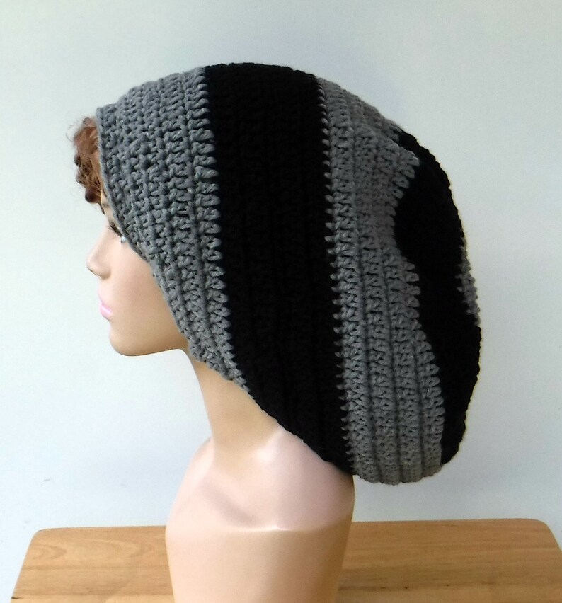 May include: A handmade crochet beanie in a striped pattern of black and gray. The hat is made of soft yarn and has a ribbed texture. The beanie is designed to be worn on the head.