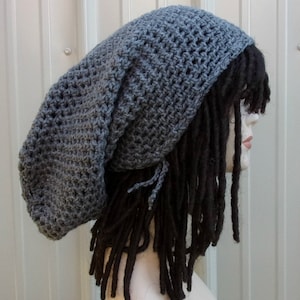 May include: A gray crochet beanie with a long, slouchy design. The hat is made of a textured yarn and features a loose weave. The beanie is shown on a mannequin head with black dreadlocks.