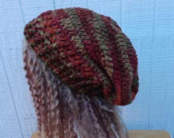 May include: A handmade crochet beanie in shades of red, orange, and green. The hat is made of thick yarn and has a textured, ribbed design. The beanie is shown on a mannequin head with long, wavy hair.
