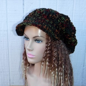 May include: A brown, green, and red crocheted beanie with a brim. The beanie is worn on a mannequin with long, brown and blonde curly hair.
