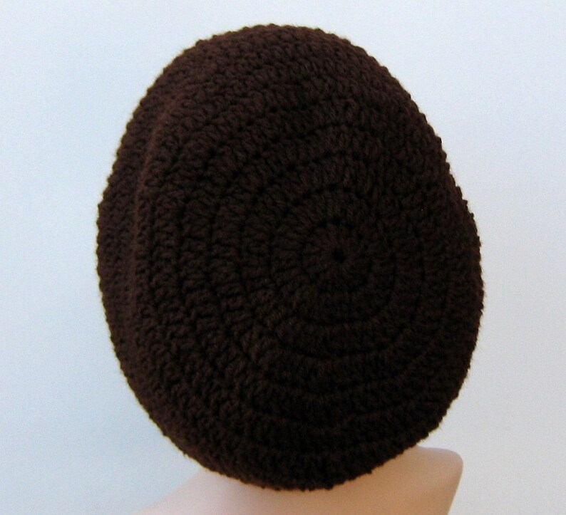 May include: A brown crocheted beanie hat. The hat is made with a simple stitch pattern and has a rounded crown.