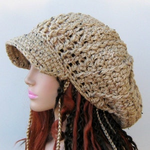 May include: A tan crochet hat with a visor. The hat has an open weave design and is made of a textured yarn. The hat is shown on a mannequin head with red and black braids.