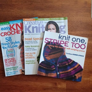 May include: Three knitting magazines with colorful covers. The top magazine is titled "Creative Knitting" and features a woman with brown hair. The middle magazine is titled "Bead Special" and features a colorful knitted scarf. The bottom magazine is titled "Knit One, Stripe Too" and features a colorful knitted hooded sweater.