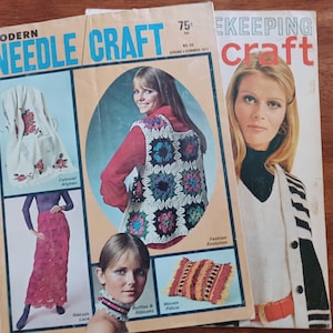 May include: Three vintage magazines with women on the covers. The magazine on the left is titled "Modern Needle Craft" and features a woman wearing a crocheted vest. The magazine on the right is titled "Keeping Craft". The magazines are on a wooden surface.