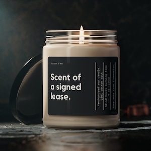 May include: A beige soy candle in a clear glass jar with a black label that reads "Scent of a signed lease." The candle is hand-poured and has a 100% cotton wick. It has a burn time of 50-60 hours and is 9 ounces (225g).