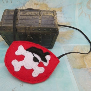 May include: A red felt pirate eye patch with a white skull and crossbones design. The eye patch has a black felt eye covering and an elastic strap.