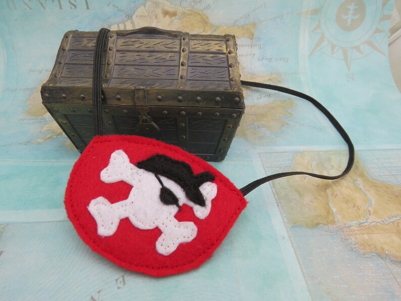 May include: A red felt pirate eye patch with a white skull and crossbones design. The eye patch has a black felt eye covering and an elastic strap.