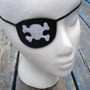 May include: A white foam mannequin head wearing a black felt pirate eye patch with a white felt skull and crossbones design.