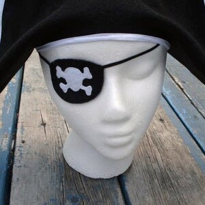 May include: A black felt pirate hat with a white trim and a black eye patch with a white skull and crossbones design.