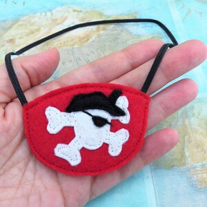 May include: Red felt pirate eye patch with a white skull and crossbones design and a black felt pirate hat. The eye patch has an elastic strap.