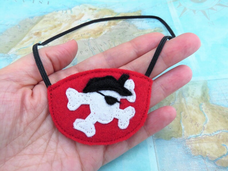 May include: Red felt pirate eye patch with a white skull and crossbones design and a black felt pirate hat. The eye patch has an elastic strap.