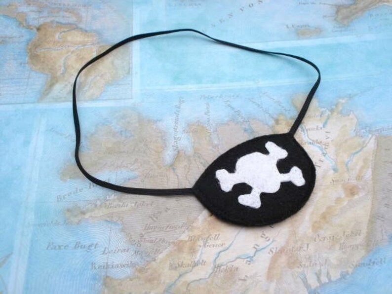 May include: A black felt pirate eye patch with a white skull and crossbones design. The eye patch is attached to a black elastic band.