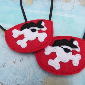 May include: Two red felt pirate eye patches with white skull and crossbones and black eye patches. The eye patches are attached to black elastic bands.