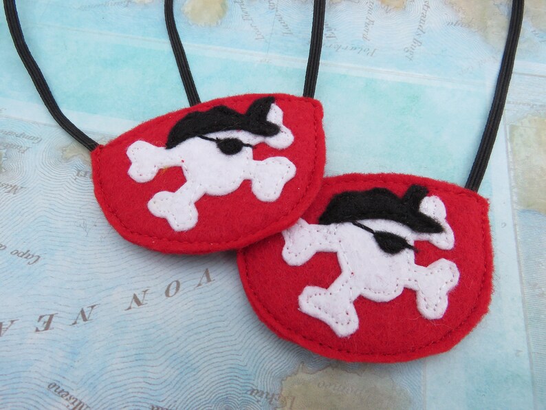 May include: Two red felt pirate eye patches with white skull and crossbones and black eye patches. The eye patches are attached to black elastic bands.