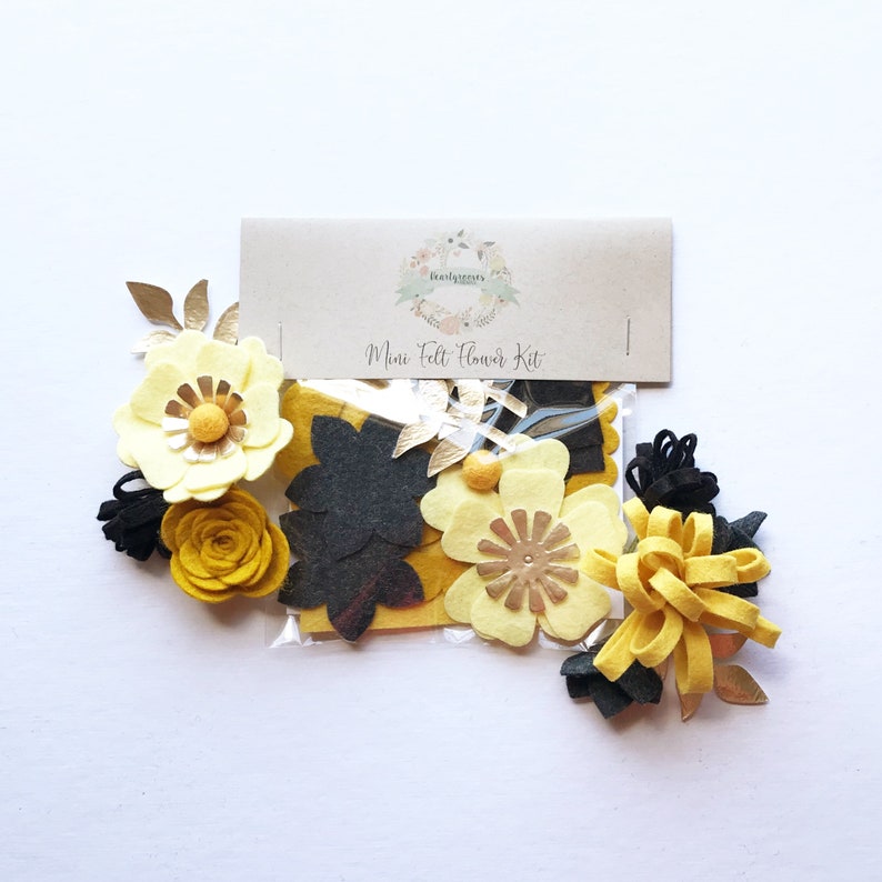 Peut inclure: Un kit pour faire des fleurs en feutre. Le kit comprend des pi&egrave;ces de feutre jaunes, noires et dor&eacute;es de diff&eacute;rentes formes et tailles. Le kit est emball&eacute; dans un sac en plastique transparent avec une &eacute;tiquette en papier brun qui indique "Mini Felt Flower Kit".