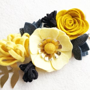 Peut inclure: Une composition florale en feutre jaune et blanc avec un centre dor&eacute;. Les fleurs sont dispos&eacute;es en rang&eacute;e et sont rehauss&eacute;es de feuilles en feutre noir.