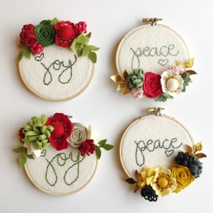 Peut inclure: Quatre cerceaux &agrave; broder avec des fleurs en feutre et les mots "joie" et "paix" brod&eacute;s dessus. Les fleurs sont dans des tons de rouge, vert, blanc, or et noir.
