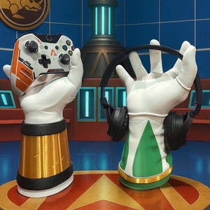 May include: Two decorative hand sculptures, one holding a white and orange video game controller, the other holding black headphones. The sculptures have gold and green accents and are set against a blue background.