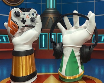 May include: Two decorative hand sculptures, one holding a white and orange video game controller, the other holding black headphones. The sculptures have gold and green accents and are set against a blue background.