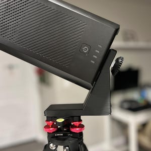 May include: A black device with a power button and indicator lights is mounted on a black tripod with red adjustment knobs. The tripod has three legs and a bubble level.