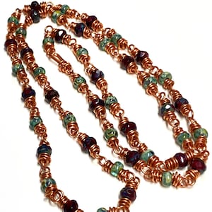 May include: A copper wire necklace with dark red and green glass beads. The necklace is made of multiple strands of wire wrapped around the beads.