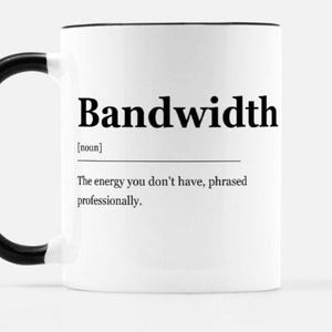 Può includere: Tazza in ceramica bianca con manico e bordo neri. La tazza presenta la parola "Bandwidth" in grassetto, in nero, insieme a una definizione: "L'energia che non hai, espressa professionalmente."