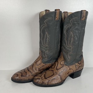 May include: A pair of cowboy boots with a snakeskin pattern on the lower part and a gray leather upper. The boots have decorative stitching and a pointed toe. The heels are black.