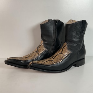 May include: A pair of black leather cowboy boots with a snakeskin pattern on the vamp. The boots have pointed toes, zippers on the sides, and a low heel. The boots are set against a white background.