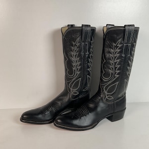 May include: A pair of black leather cowboy boots with decorative stitching in a light color. The boots have a pointed toe and a tall shaft, suitable for riding or Western-themed attire.
