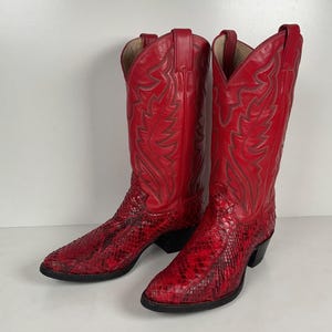 May include: A pair of vibrant red cowboy boots featuring a textured snakeskin-patterned leather vamp and a smooth leather shaft with intricate tonal stitching details. The boots have a pointed toe, a stacked heel, and pull tabs at the top edges.