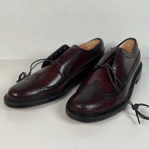 May include: A pair of burgundy leather wingtip dress shoes with black soles and laces. The shoes have decorative perforations and are displayed on a white background.
