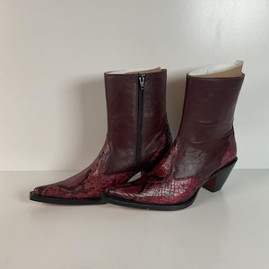 May include: A pair of burgundy ankle boots with a snakeskin pattern on the lower portion and a solid burgundy upper. The boots have a pointed toe, a black zipper, and a black heel.