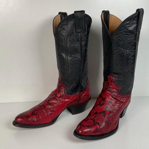 May include: A pair of tall cowboy boots featuring black leather shafts with decorative stitching and red snakeskin-textured vamps. The boots have pointed toes, stacked heels, and pull tabs at the top of the shafts, showcasing a two-tone design.