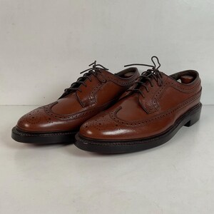 May include: A pair of brown leather wingtip dress shoes with dark brown laces. The shoes have a classic design with decorative perforations and a sturdy sole. The shoes are displayed on a white surface.